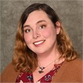 Katie Clark, Admin Assistant to ESBS Dean a smiling woman, Katie Clark, with long wavy red hair, wearing a orange-brown cardigan and patterned red blouse