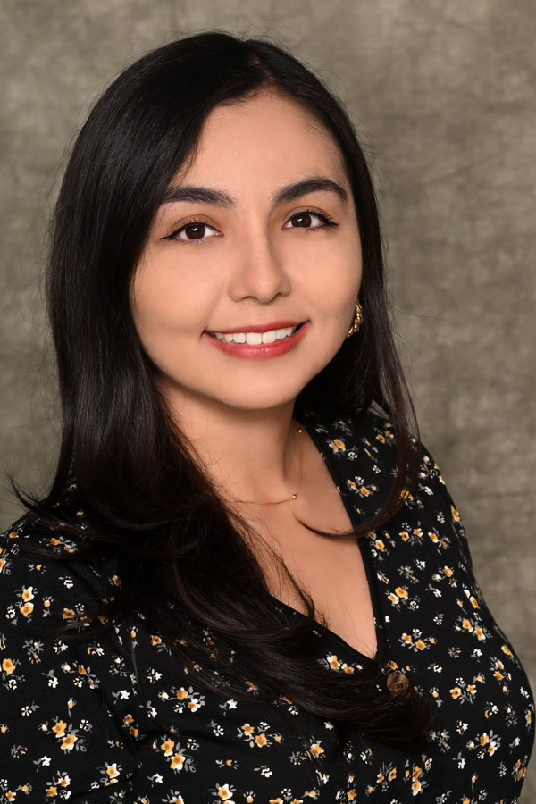 Vanessa Rodriguez a smiling young woman, Vanessa Rodriguez, with long dark hair, wearing a black floral blouse and a gold choker