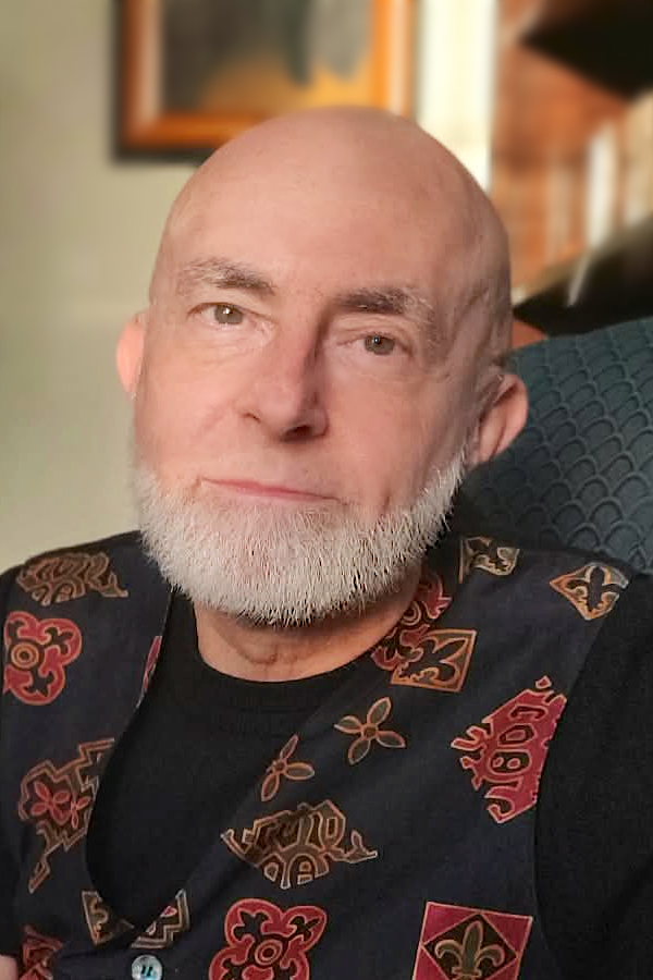 Karl Sherlock photograph of a bald man, Karl Sherlock, with a white beard, a black shirt, and a patterned vest with gold and jewel-tone designs