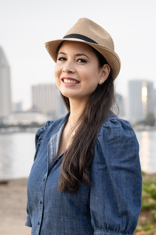 Daniela Sow Photograph of a smiling woman, Daniela Sow, with long hair and wearing a tan fedora hat and a blue denim shirt.